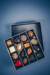 Small square box of chocolate pralines and truffles assorted. Different shapes and fillings. Blue toned background, directly above.
