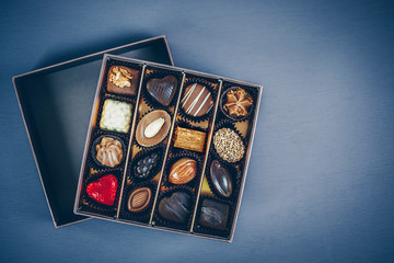 Small square box of chocolate pralines and truffles assorted. Different shapes and fillings. Blue toned background, directly above.
