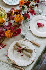 Autumn table setting with beautiful plates, pumpkins and and flowers, fall home decoration for festive dinner.