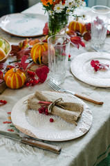Autumn table setting with beautiful plates, pumpkins and and flowers, fall home decoration for festive dinner.