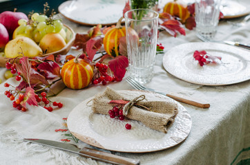 Autumn table setting with beautiful plates, pumpkins and and flowers, fall home decoration for festive dinner.