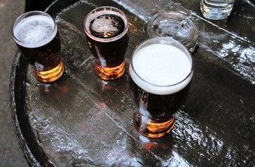 Three pints of lager beer viewed from above on a brown barrel outside of a pub or a bar, and an ashtray