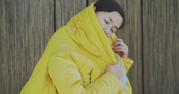 Outdoors fashion portrait of trendy pretty asian girl posing on the wall background. Woman smiling and walking on the city. Wearing stylish wide jeans and long yellow jacket. 4k video