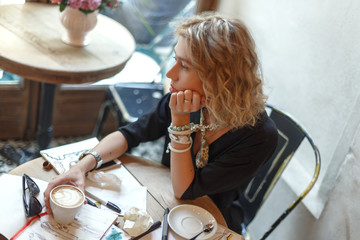 A young girl in a cafe drinks coffee and draws sketches of clothes