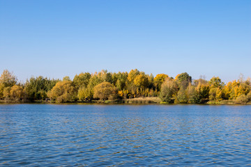 Lake and golden trees on blue sky background