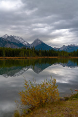 The foothills of the Rockies reflecting in an alpine lake as a moody storm roles in