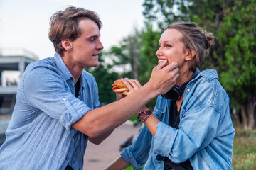 Obraz premium Lovely young hipster couple dating during summer sunset. they wear jeans clothes. they eat burger fastfood together