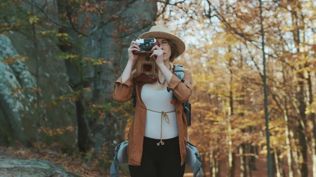 Portrait shot of beautiful young woman in hat taking pictures in the old vintage camera and smiling