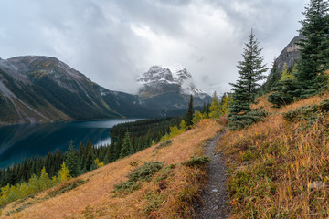 A trail follows the ridge above a blue alpine lake in the Rockies