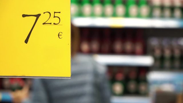 Price tag on shelves supermarket. Young woman shopping at background