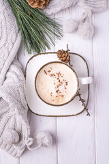 Obraz na płótnie Canvas Coffee cappuccino with ceylon cinnamon, a branch of a pine tree and knitted accessories on a white wooden background
