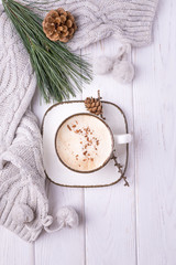 Fototapeta na wymiar Winter mood. Coffee cappuccino with ceylon cinnamon, a branch of a pine tree and knitted accessories on a white wooden background