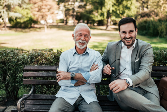 Portrait of a business family outdoors. Two men sitting in the park looking at camera.