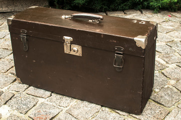 Old used weathered vintage grunge suitcase on stone pavement closeup in house backyard