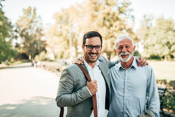 Outdoor portrait of two elegant men. Senior and young man smiling and looking at camera. - obrazy, fototapety, plakaty