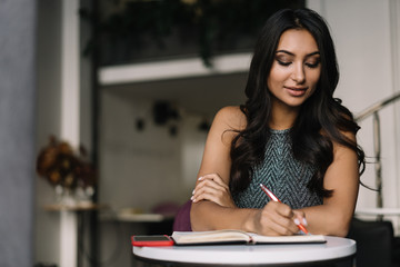 Cheerful Indian university student studying at library, learning English language, write notes, exam preparation, working project. Portrait of beautiful asian woman sitting at table and smiling. 