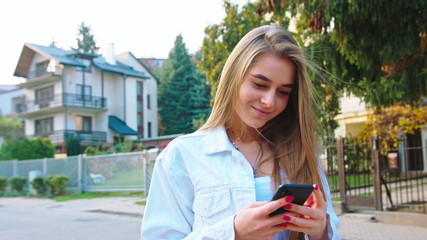 Woman texting on smartphone looking happy outside, Caucasian girl in her 20s happily texting on...