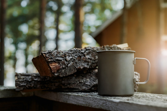 A metal cup for camping on the background of a wooden house at sunset.