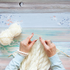 A woman knits a white knitted fabric of woolen yarn. Coffee black. Pastry macaroons. An old background of pastel color.