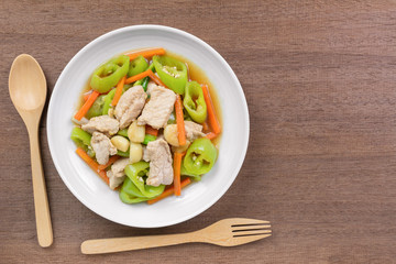 top view of stir fried pork with banana pepper in a ceramic dish on wooden table. hot and spicy homemade style food concept.