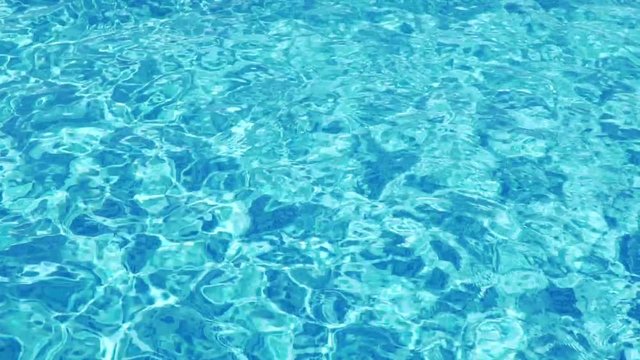 Slow motion background of a pool with wavy clean fresh water at sunset of the day. Reflection of clear blue pool water, flashes. Texture bright turquoise surface of the water in the pool