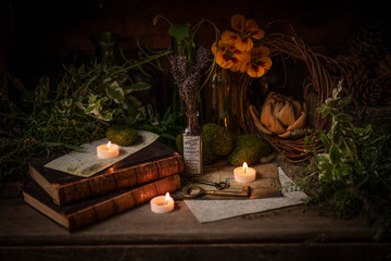 Still life with old books, candles and herbs with flowers.