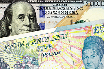 A close up image of a five pound note from England with a blue, American one hundred note