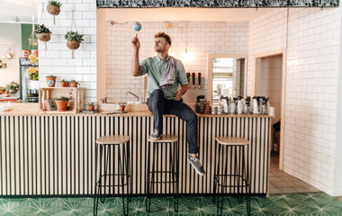 Young man working in his start-up cafe, spinning a little globe on his forefinger