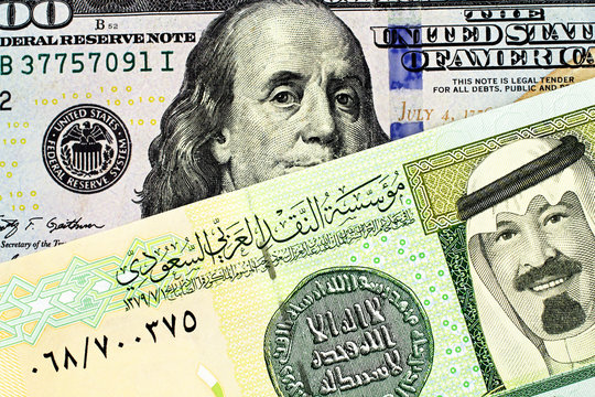 A close up image of a blue American one hundred dollar bill and a Saudi Arabian one riyal note