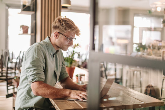 Young man working in his start-up cafe, using laptop