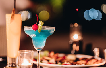 Blue cocktail on the glass with the bbq food in the night dinner party