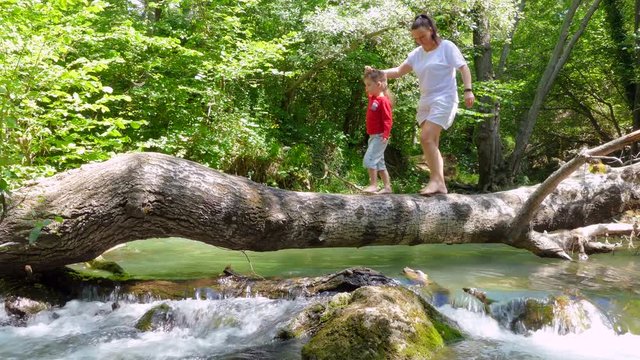 Mom and Son are walking on a log that fell across the river to sit on it.
