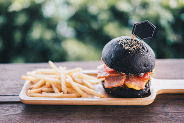 Charcoal burger made with black charcoal bun with sesame served with potato french fries on wooden...