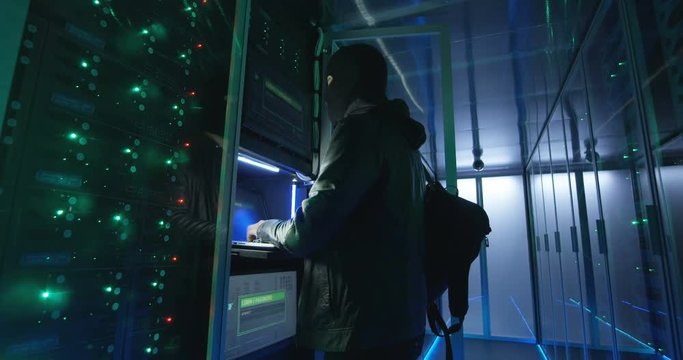 Wide view of bearded man in black using computer and hacking servers of data center launching DDoS attack