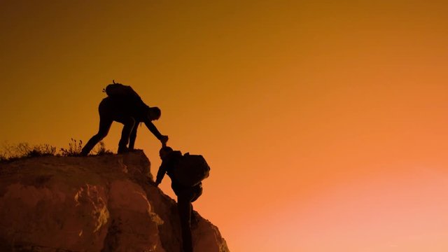 silhouette two men teamwork tourists climber climbs a mountain. walking tourist hiking adventure climbers sunset climb the mountain . slow motion video lifestyle . hiker sunlight on top win victory