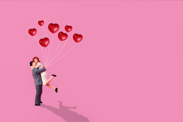miniature couple standing and holding red love balloon in pink background