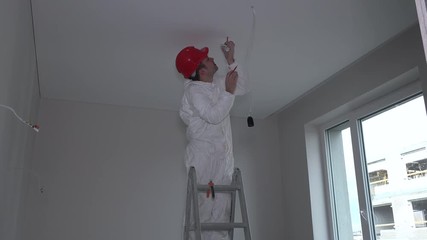 Man on ladder installing smoke detector on room ceiling