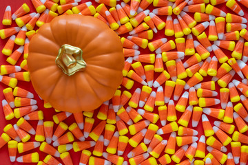 Fototapeta premium Big pile of Halloween candy corn on an orange background, with a ceramic orange pumpkin 