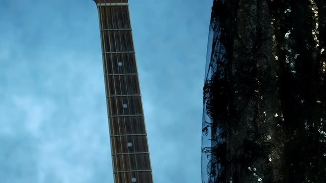 Close-up of a feminine hand on the fretboard of an acoustic guitar. The girl in the concert dress comes up and gently moves her fingers up the strings. Smoke in the background. Theme for music video.