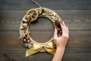 Hand hang a creative christmas wreath made of thread, dry fruits and nuts on dark wooden background top view copy space
