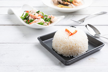 Steamed Thai jasmine rice in black plate with paco fern spicy salad and tom yum sea food