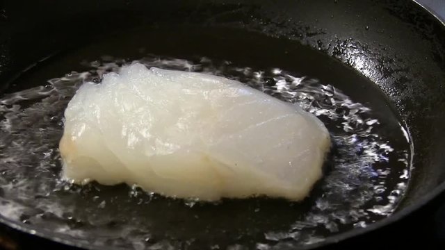 A piece of cod getting fried in a pan
