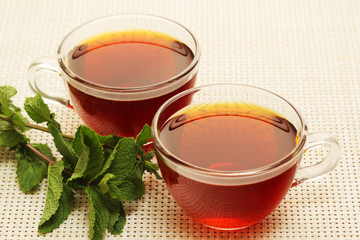 Two cups with black tea with fresh leaves of mint