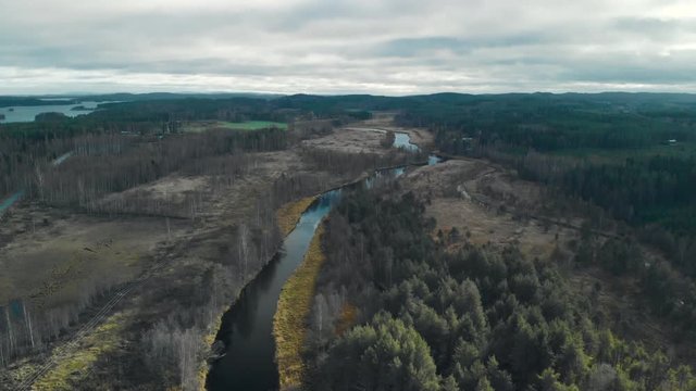 Aerial, descending, tilt, drone shot, of a river, surrounded by leafless, autumn forest. There¬¥s some sunlight, on a cold, cloudy, fall day, in Juuka, North Karelia, Finland