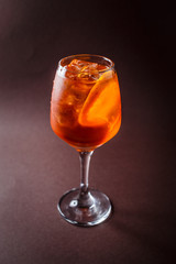 Glass of Aperol Spritz with orange on elegant dark brown background