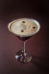 Glass of espresso martini with coffee beans and vodka on elegant dark brown background