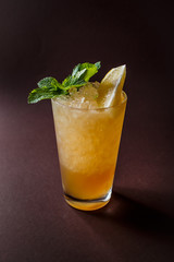 Glass of orange cocktail with mint, ice and slice of orange on elegant dark brown background