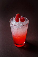 Glass of red coctail with ice and raspberry on elegant dark brown background