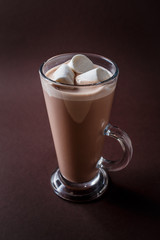 Glass of cacao with three marshmallows on elegant dark brown background