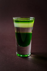 Green alcoholic shot glass with absent, irish cream, liquor on elegant dark brown background